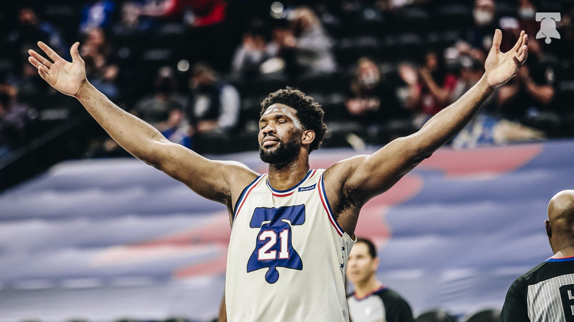 Joel Embiid standing with his hands raised wide open.